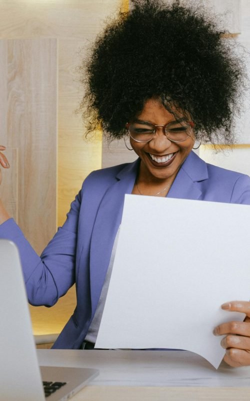 lady smiling looking at paperwork in front of computer desk