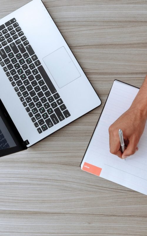 overlook of lady at desk writing something down in notebook and laptop in view